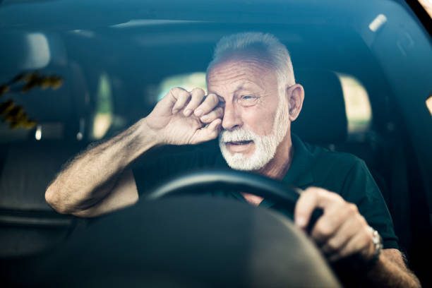 Personne âgée conductrice au volant de face se frottant l’œil gauche endormissement Aide aux victimes et familles des accidentés de la route